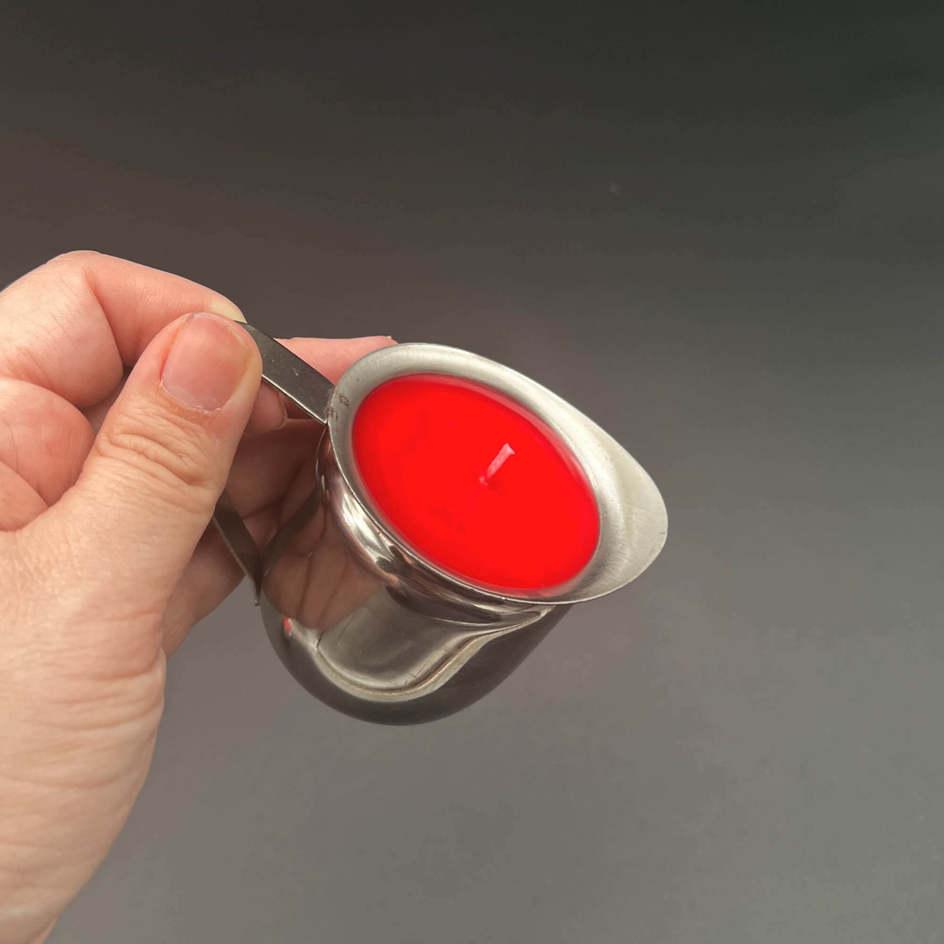 Hand holding a metal container with Red Paraffin Wax Play Candle, featuring vibrant red wax.