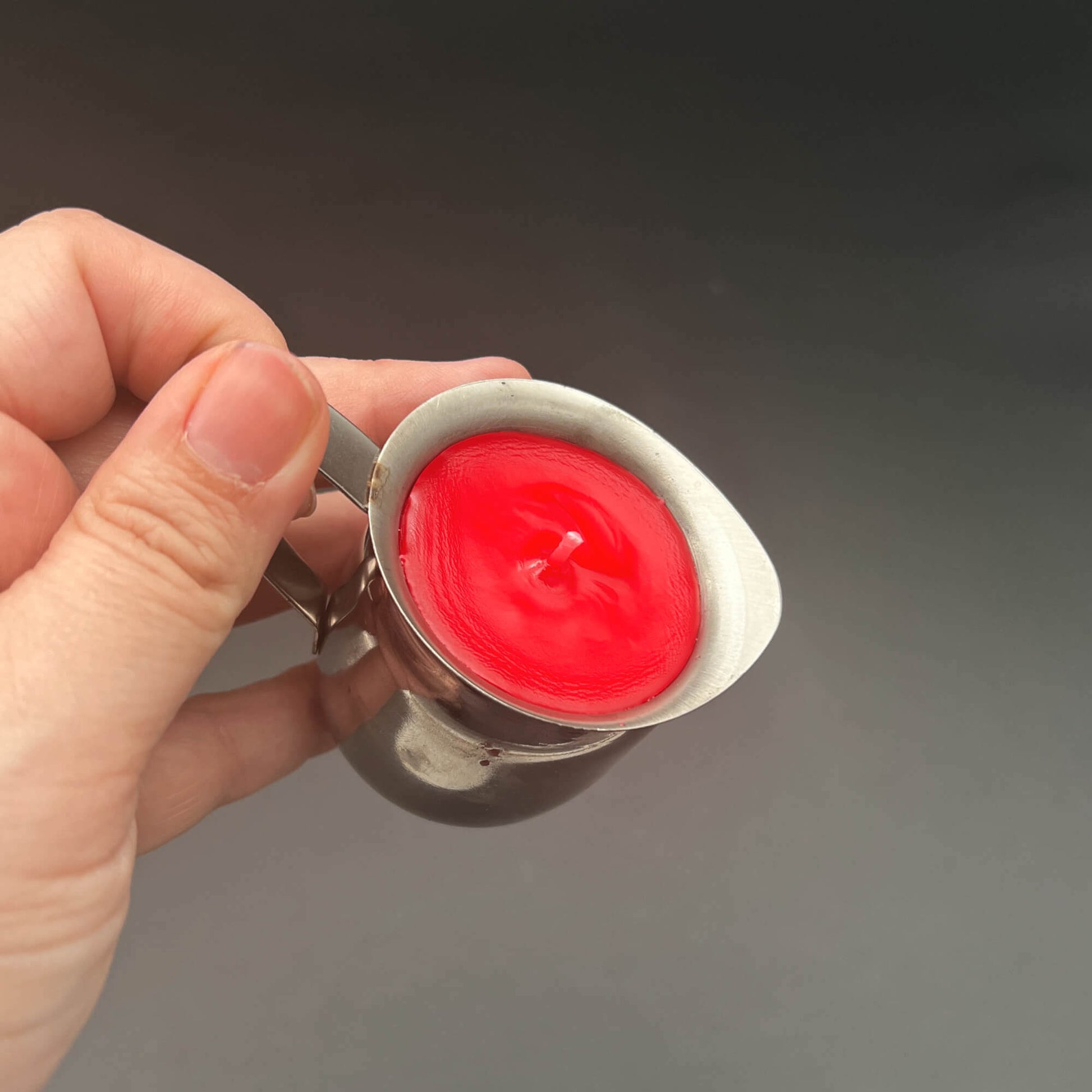 Red Paraffin Wax Play Candle in a hand, showcasing its vibrant red color and hand-poured design.