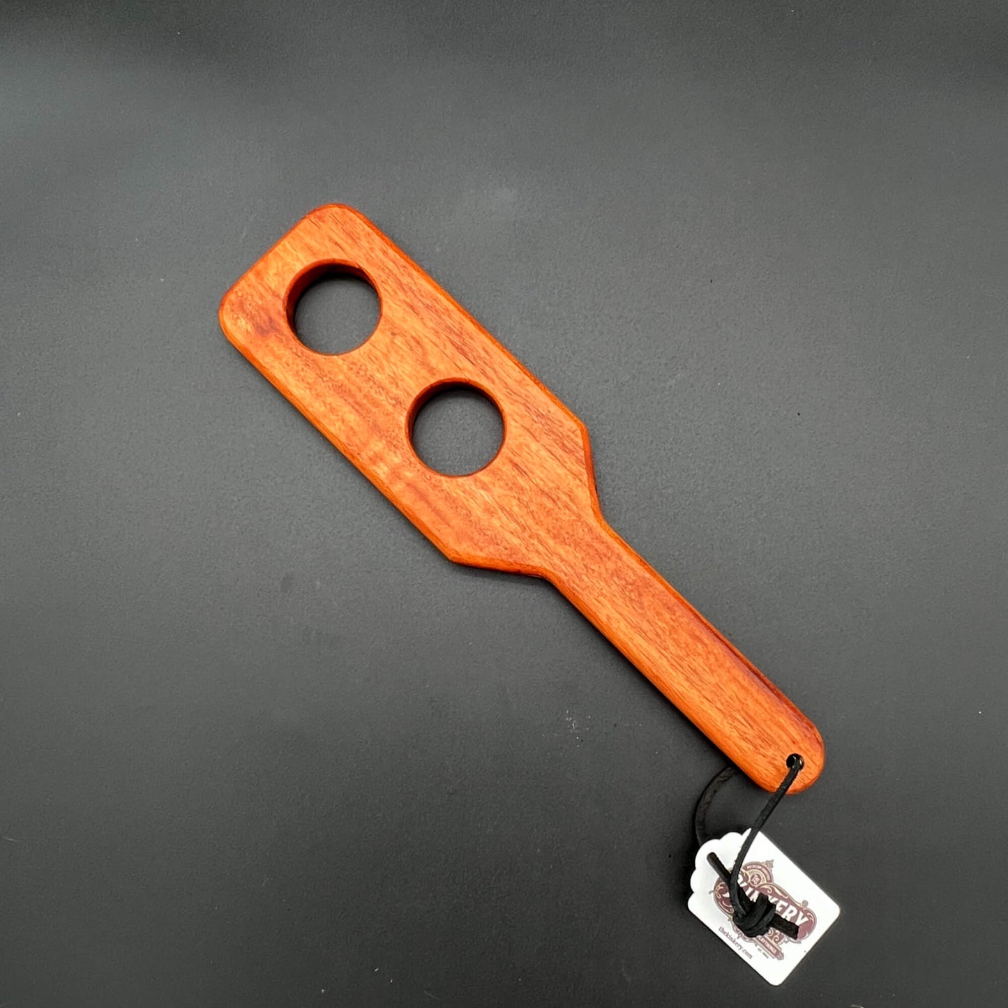 Wooden paddle with two holes on a gray background