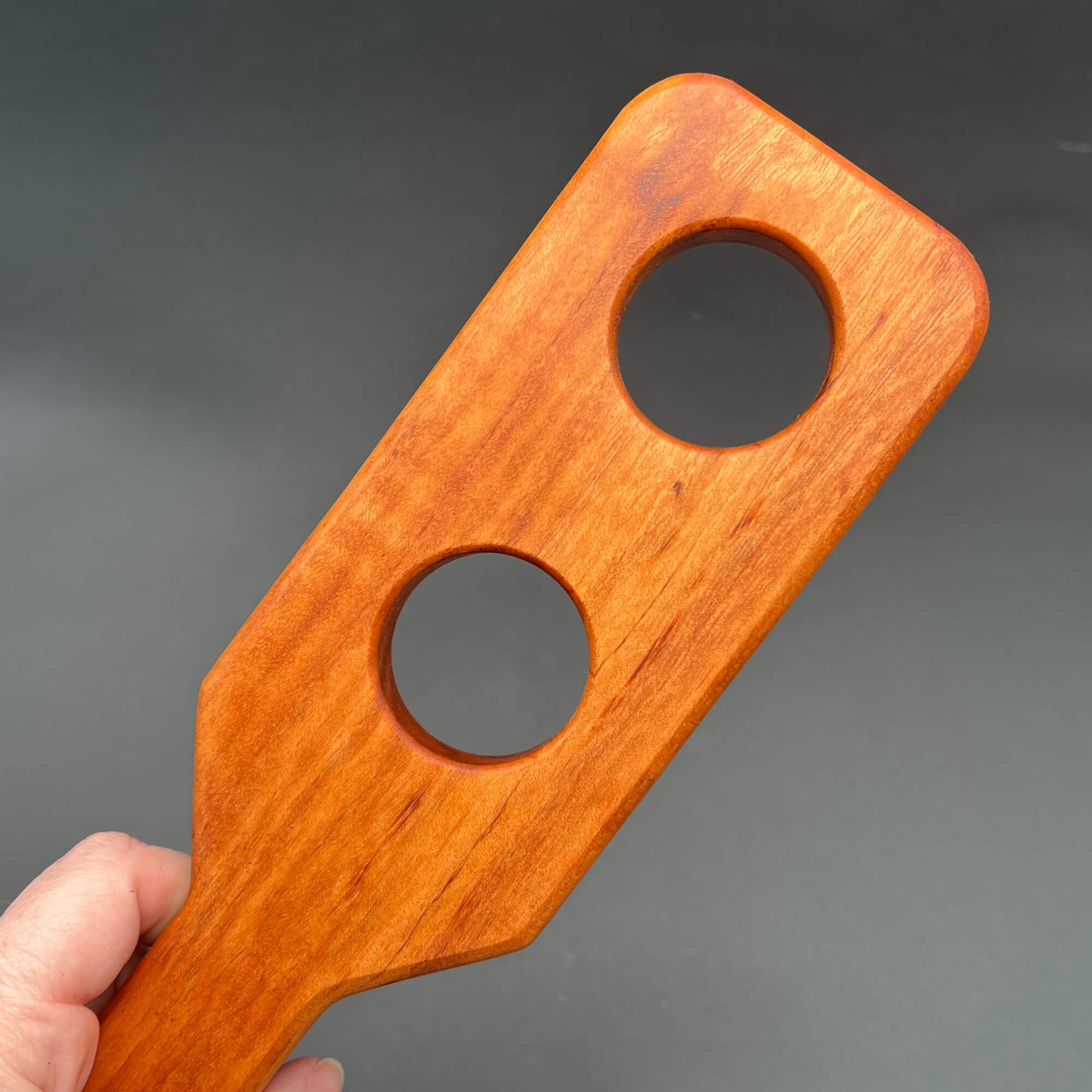 Close-up of a Holy Terror wooden paddle designed for impact play, showcasing its distinctive shape and two holes.