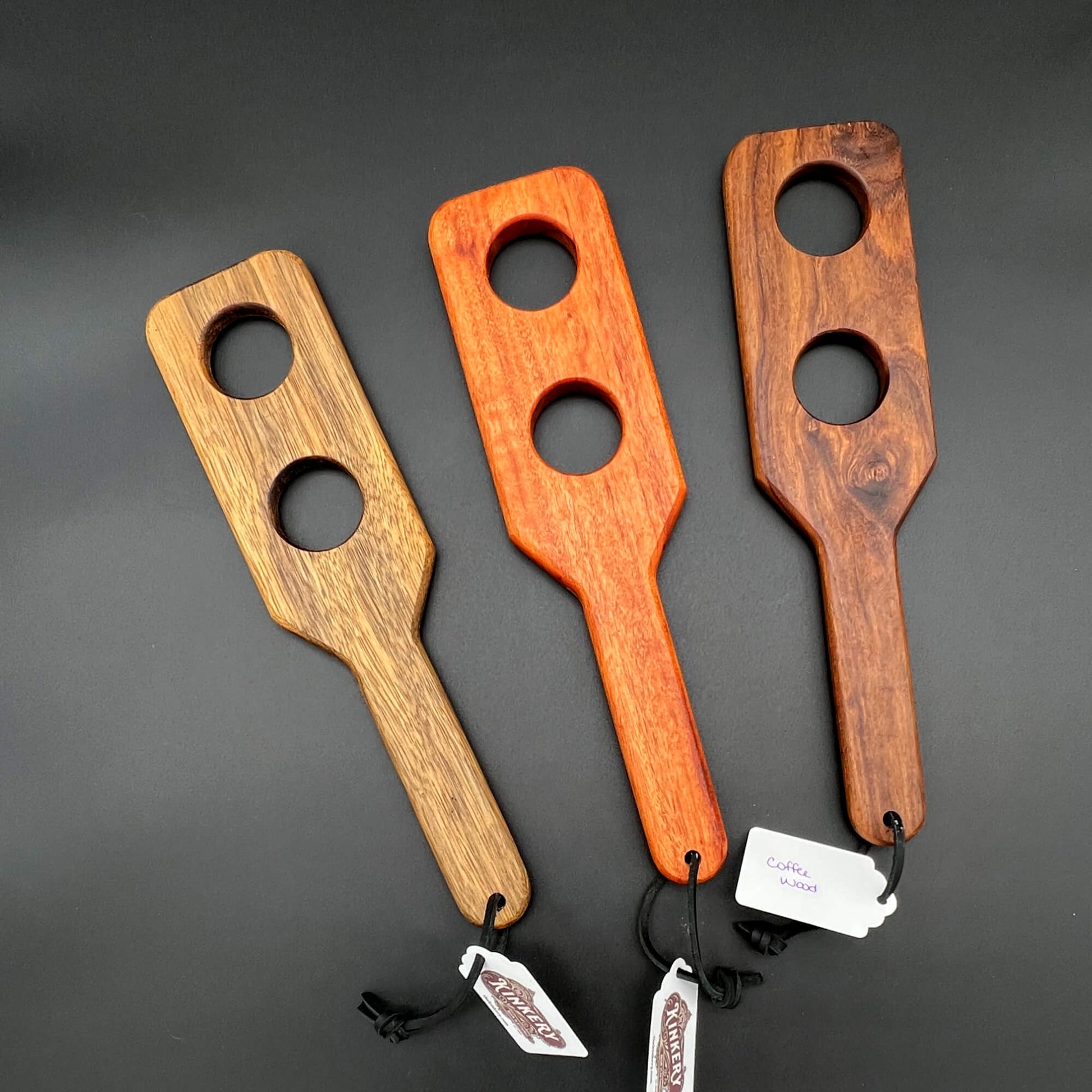 Three unique wooden paddles, called Holy Terrors, showcasing different woods each with two holes in the paddle area