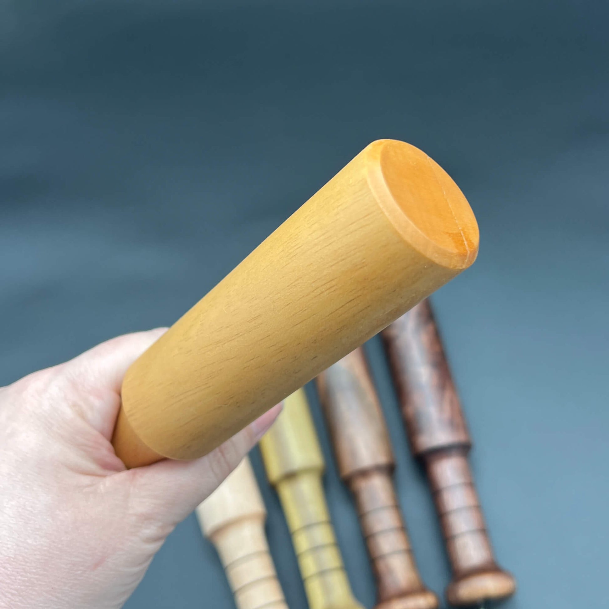 A person holding the Mini Thumper, a small thuddy paddle, with other wood paddle variations in the background.