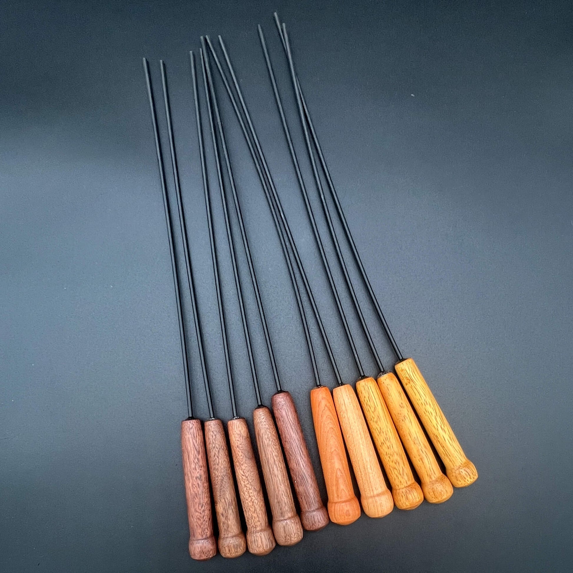 10 mini Delrin canes lined up side by side. The first five on the left have dark brown wooden handles. The next two have an orange-brown handle. The final three on the right have yellow-brown handles. They all have 3mm black Delrin rods. Each mini Delrin cane is about 13 inches long.