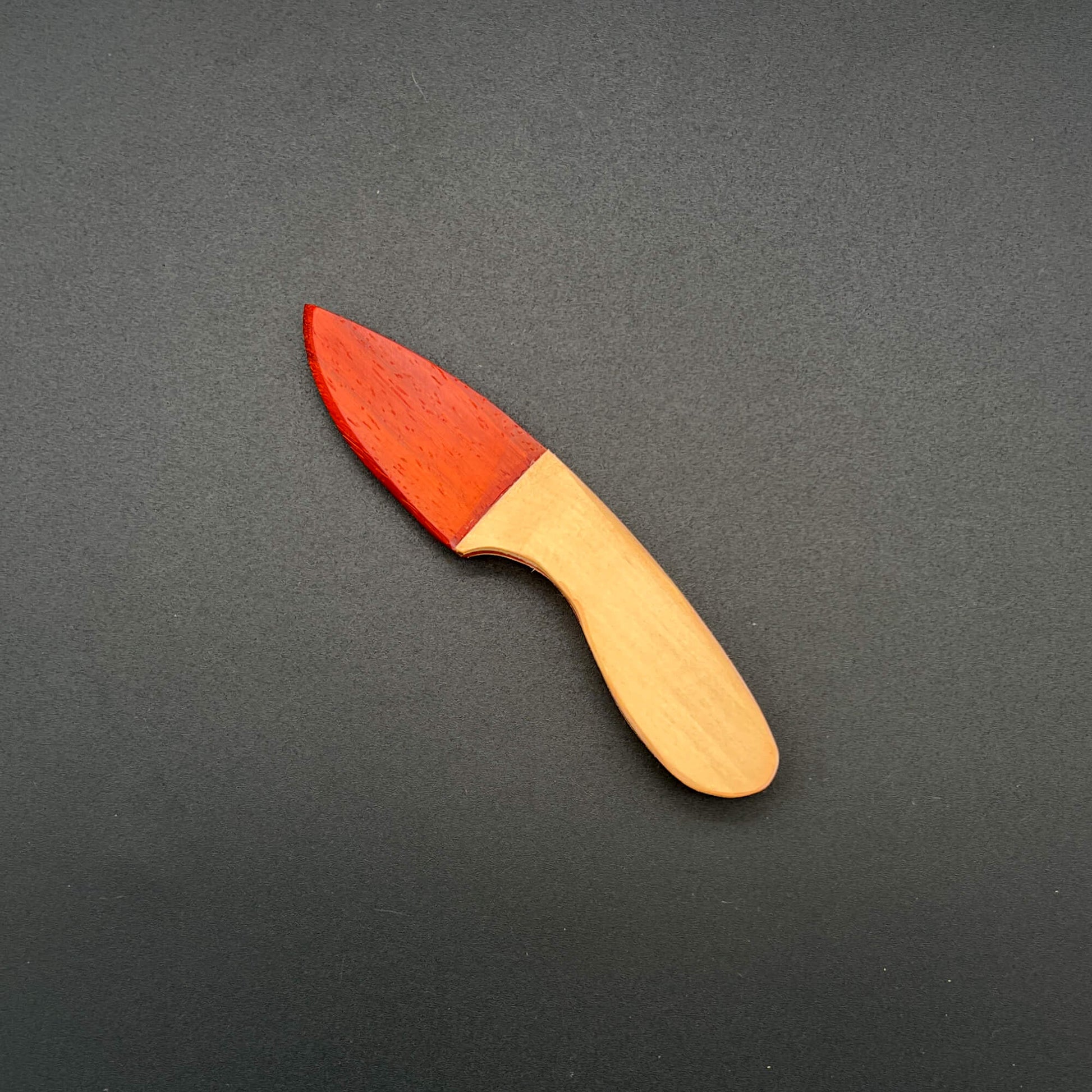 Skinner Wooden Knife with Paduak, a bright red wood blade and light maple handle on a black background.