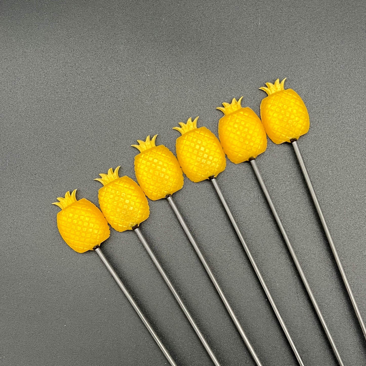 A set of seven yellow Pineapple Diabolical Sticks with sharp tips, resting on a dark surface.