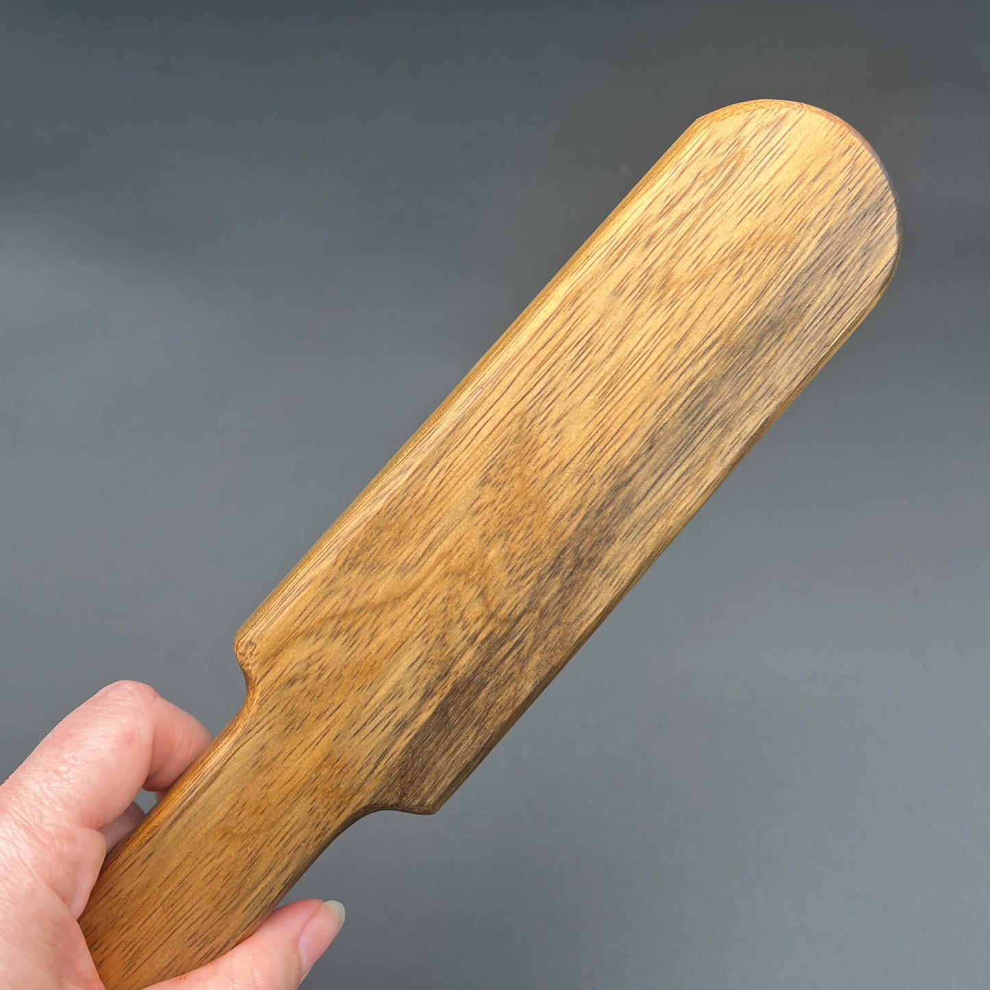 Hand holding a wooden paddle called Pounder, showcasing its natural wood finish and design.