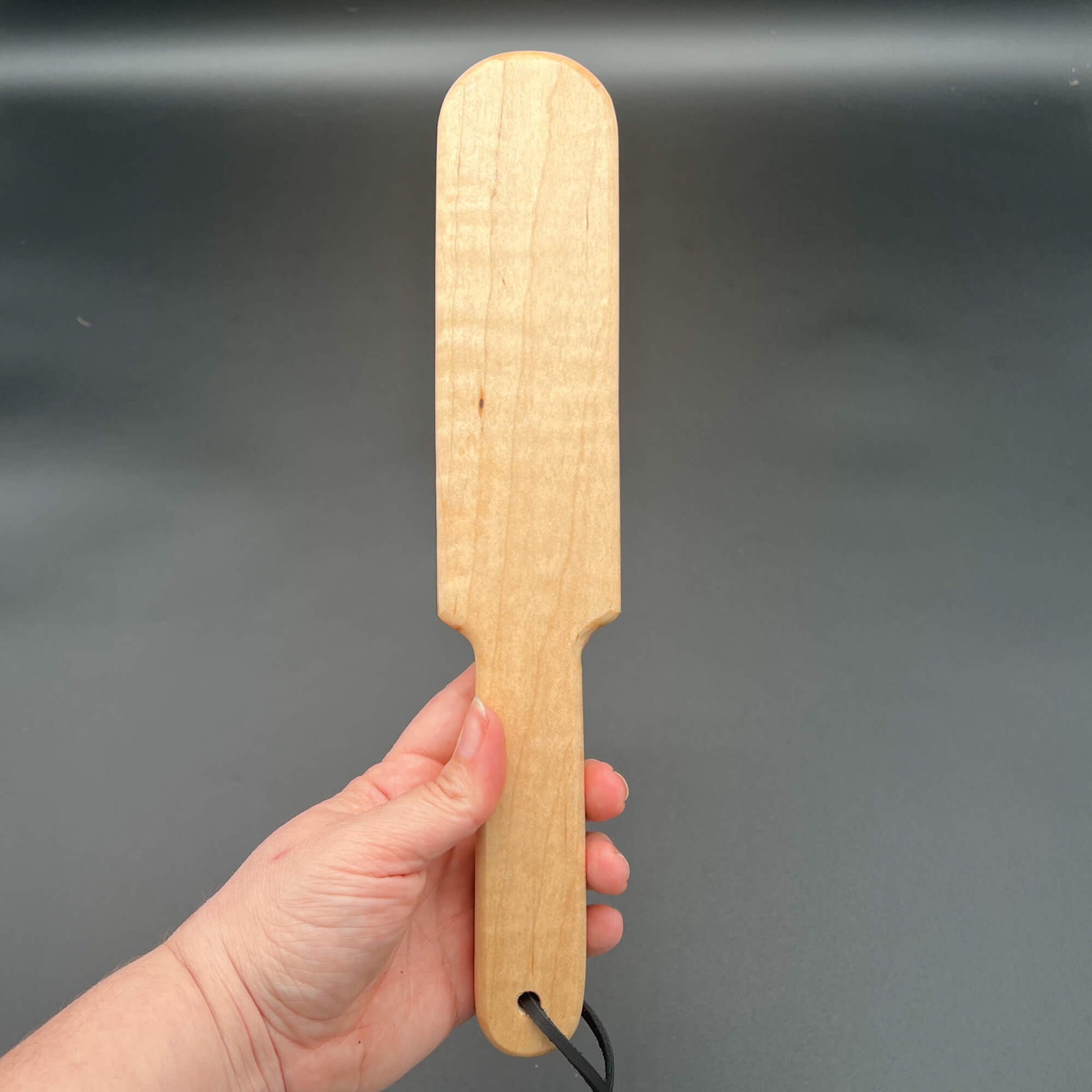 Pounder wooden paddle held in hand, showcasing natural wood grain and finish, 12 inches long and 2.25 inches wide.