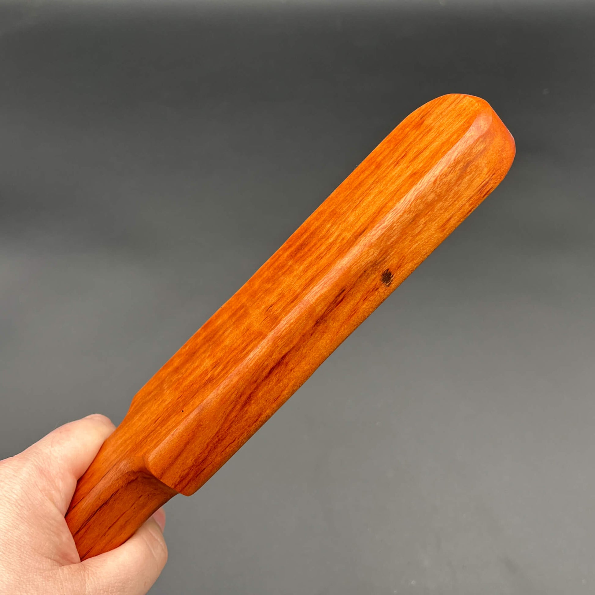 Hand holding a vibrant orange wooden Pounder paddle, a simple paddle for serious impact.