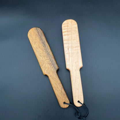 Two wooden paddles, the Pounder, showcasing natural grain and wax finish, ideal for playful spanking.
