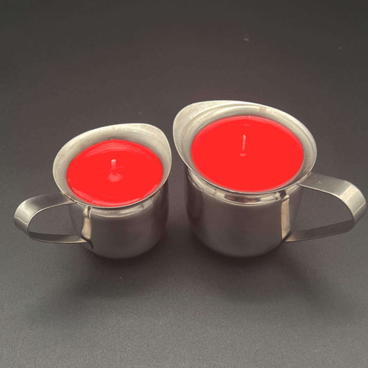 Two red paraffin wax play candles side by side. Both are in a stainless steel container with a pour spout and handle. The candle on the left is the 3 ounce (by volume) size, and the candle on the right is the 5 ounce (by volume) size.