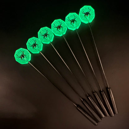 Close up of multiple glow in the dark spider webs with a black spider on top in the dark, glowing green