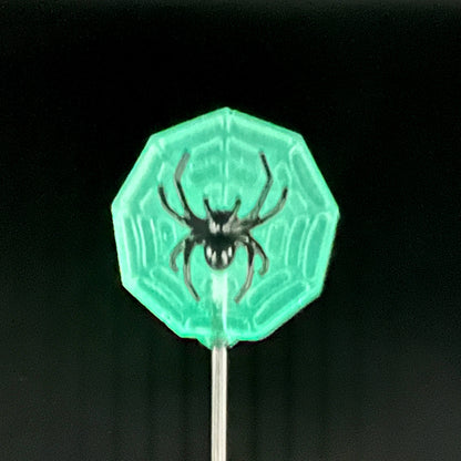 Close up of a single glow in the dark spider web with a black spider on top - in the dark, glowing green