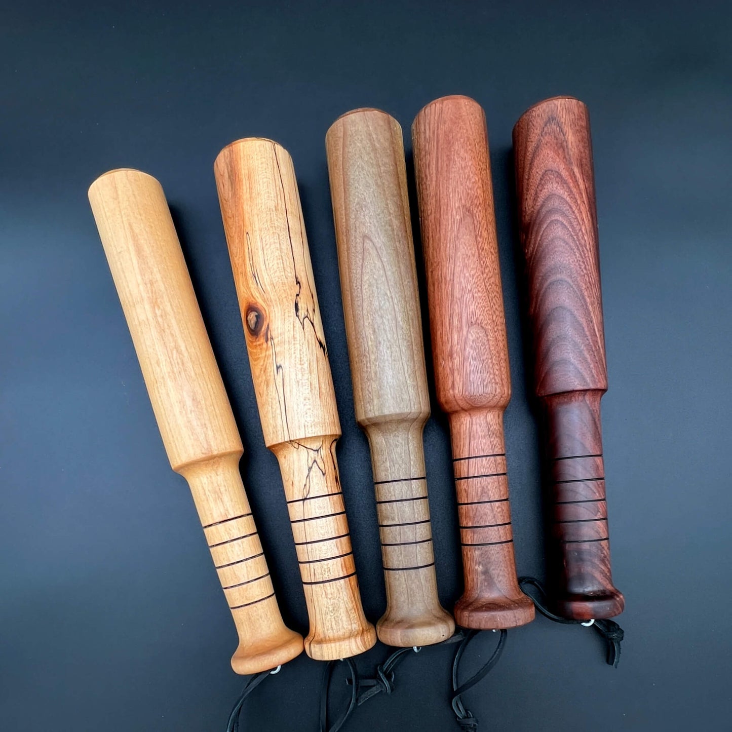 Five wooden Thumper paddles showcasing different finishes for thuddy impact play.