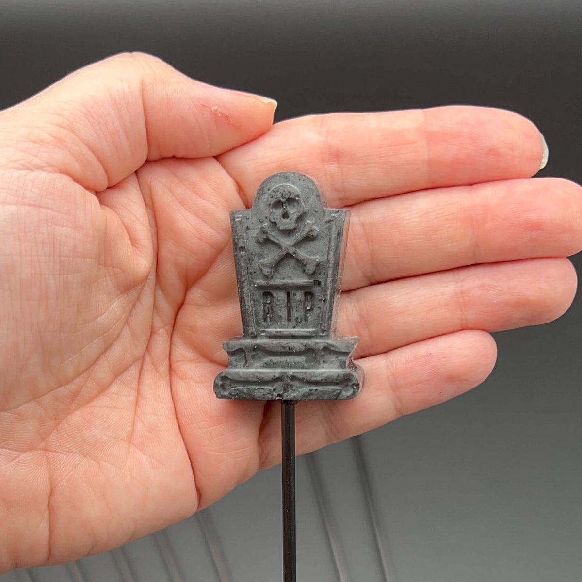 Hand holding a Tombstone Diabolical Stick with RIP design and skull & crossbones. 