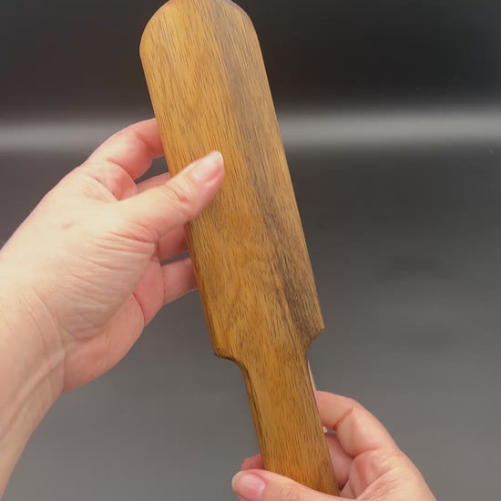 Person holding a wooden paddle, Pounder, showcasing its natural finish and sleek design as well as the smacking sound it makes