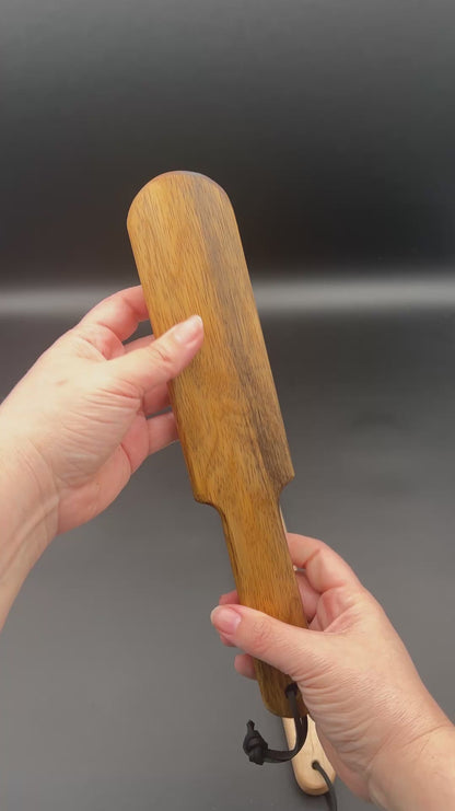 Person holding a wooden paddle, Pounder, showcasing its natural finish and sleek design as well as the smacking sound it makes