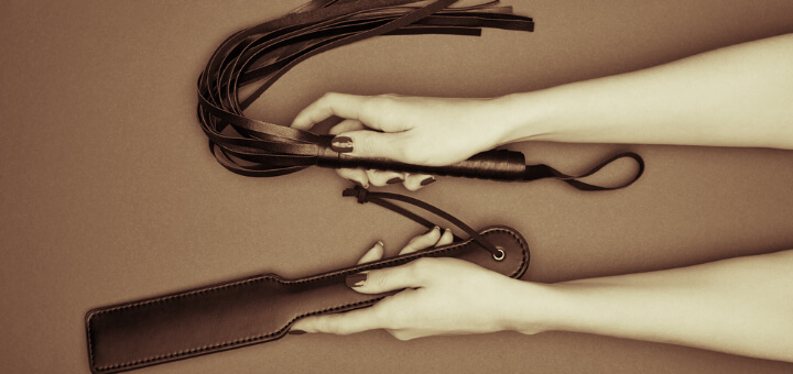 feminine hands holding leather paddle and flogger in sepia tones