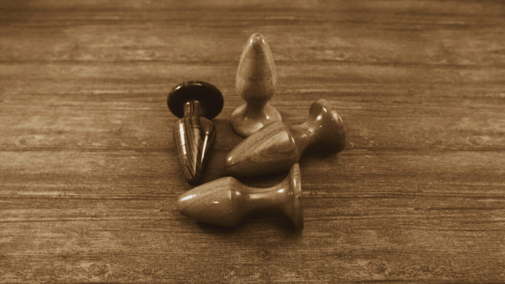 sepia tone image of four wooden butt plugs of varying sizes on wooden background