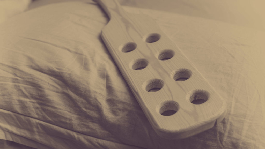 image of wooden paddle with holes on side of bed in sepia tones to indicate safety tips for using a paddle