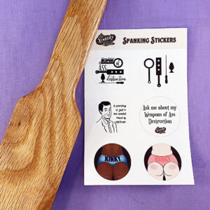 spanking sticker sheet next to wooden paddle on purple background