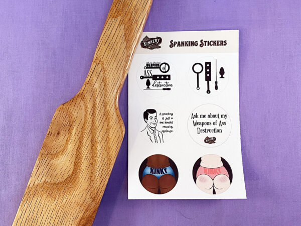 spanking sticker sheet next to wooden paddle on purple background