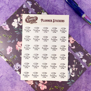 it's fine planner sticker sheet on top of purple floral planner next to pen on purple background