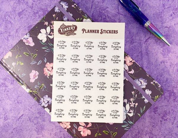 it's fine planner sticker sheet on top of purple floral planner next to pen on purple background