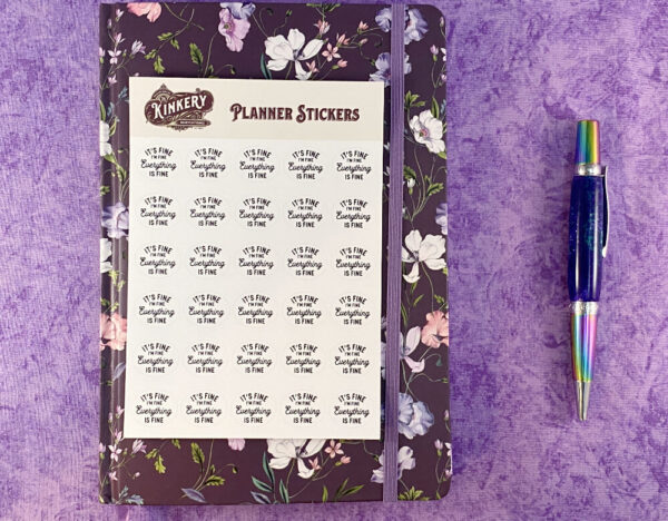 second view of it's fine planner sheet on top of purple floral planner next to turquoise pen on purple background