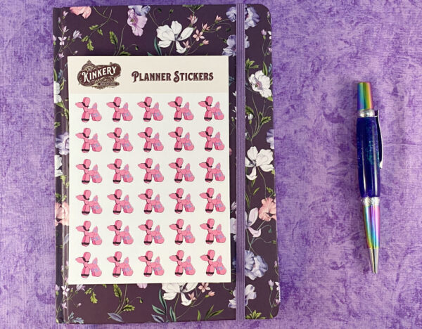 sheet of pink bondage balloon animal planner stickers on top of floral purple planner next to turquoise pen on purple background