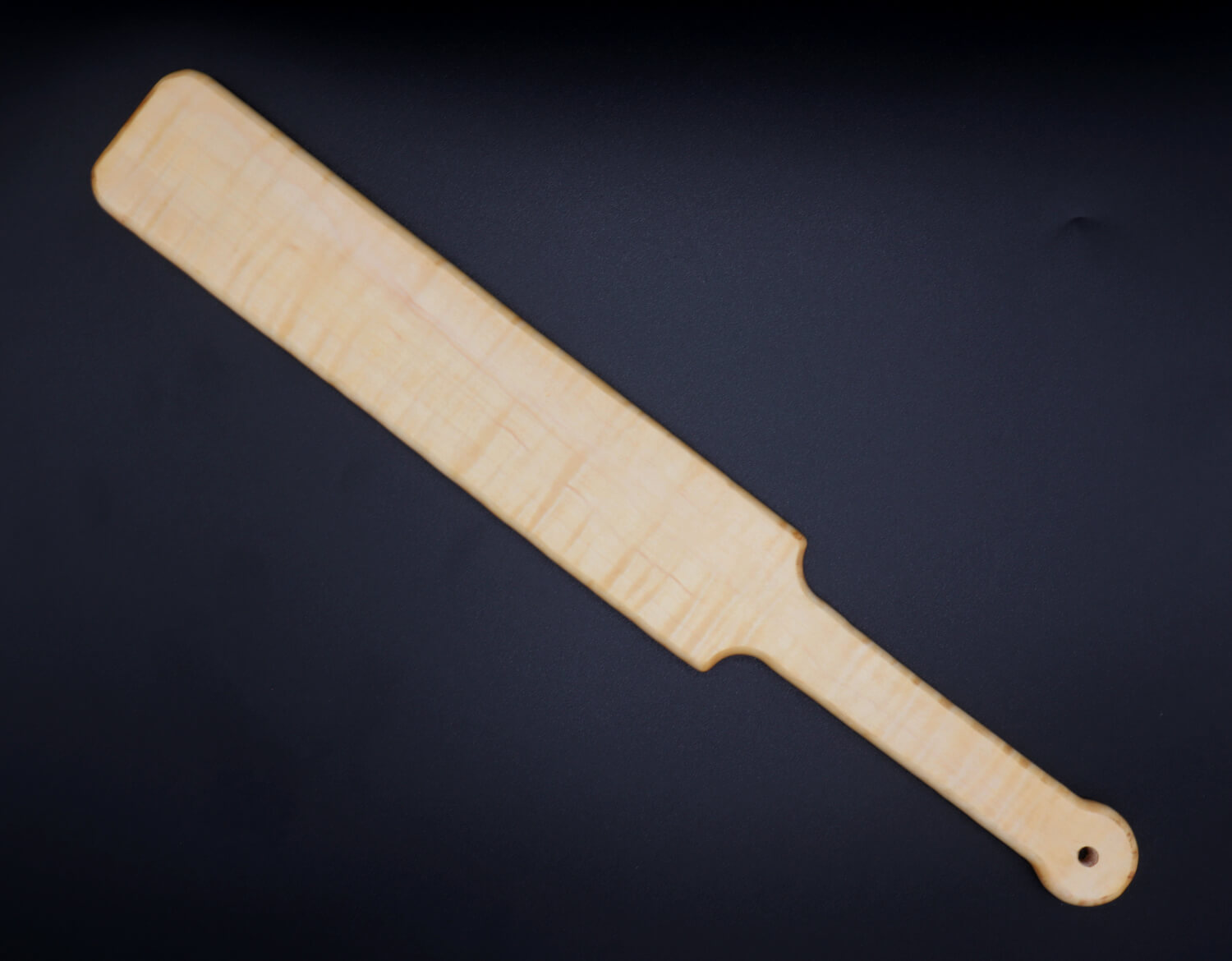large wooden paddle made of curly maple over black background
