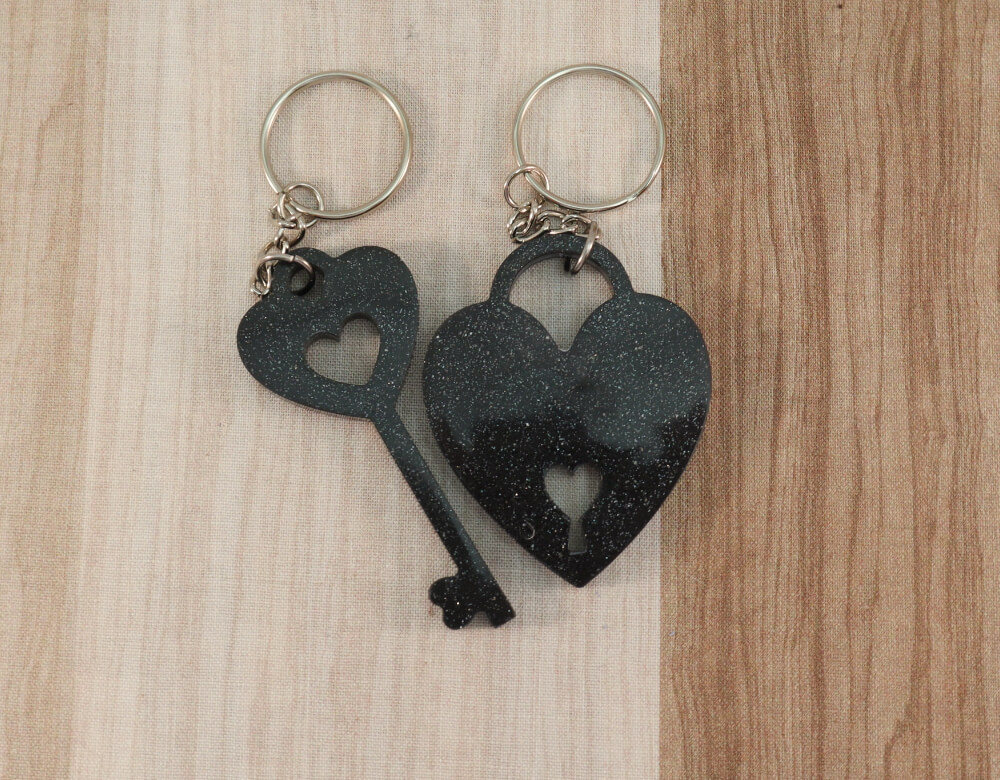 two keychain set in black resin with silver glitter; keychain on left is a key with a heart at the top; the keychain on the right is in the shape of a heart with a lock cut-out at the bottom