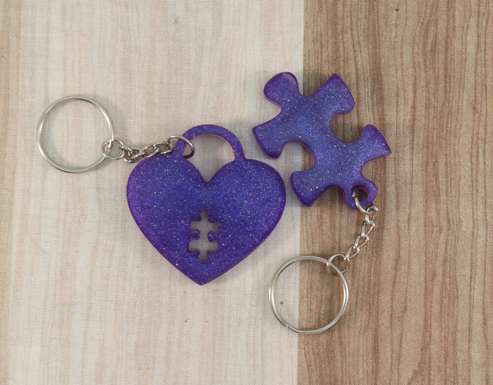 two keychain set in purple resin with purple glitter; keychain on right is a puzzle piece; keychain on left is a heart lock with a puzzle piece cut-out