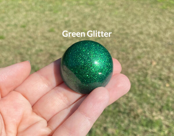 Kayla holding the green glitter resin sample in natural light over green grass