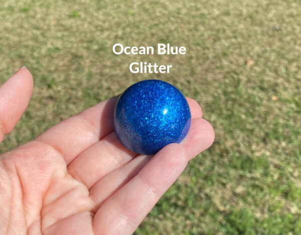 Kayla holding the ocean blue glitter resin sample in natural light over green grass