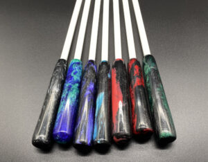 seven 3/8" white delrin canes with resin handles lined up next to each other; from left to right the colors are silver and black, blurple and turquoise, purple and black, blue and black, pink and black, red and black, green and black
