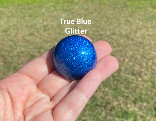 Kayla holding the true blue glitter resin sample in natural light over green grass