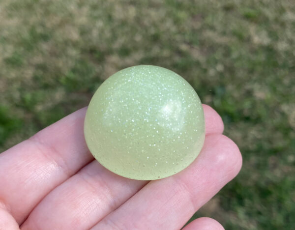 Kayla holding glow in the dark resin sample in natural light over green grass