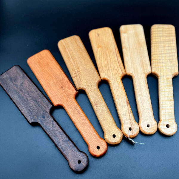 Variety of wooden paddles known as ass beater juniors. Woods from left to right: black walnut, cherry, black locust, spalted maple, maple, and curly maple