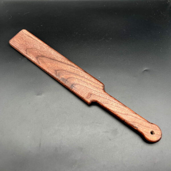 Single Ass Beater wooden paddle (18 inches long, 2.5 inches wide, .75 inches thick) in black walnut, a deep dark brown with a grain pattern of lighter and darker browns.