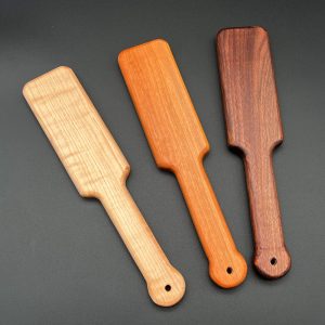 3 Ass Beater Jr paddles in different woods. Left to right: maple, a cream brown; cherry, a red-orange; and black walnut, a deep dark brown