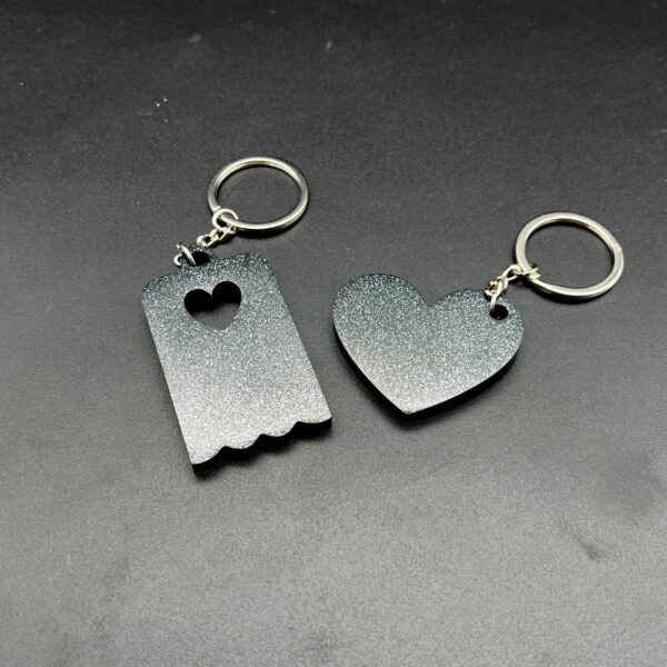 Two keychains made with black resin and silver glitter. On the left is a rectangular keychain with a scalloped bottom. On the right is a heart. Both have keychain hardware.