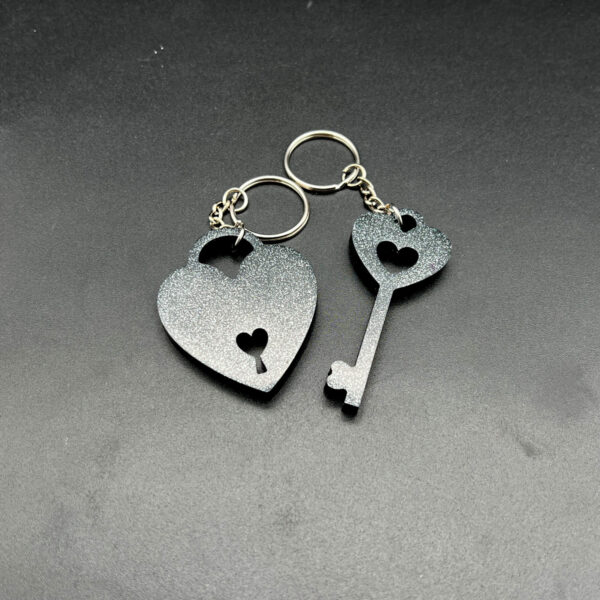 Two keychains made with black resin and silver glitter. On the left is a heart with a lock cut out at the bottom. On the right is a key. Both have keychain hardware.