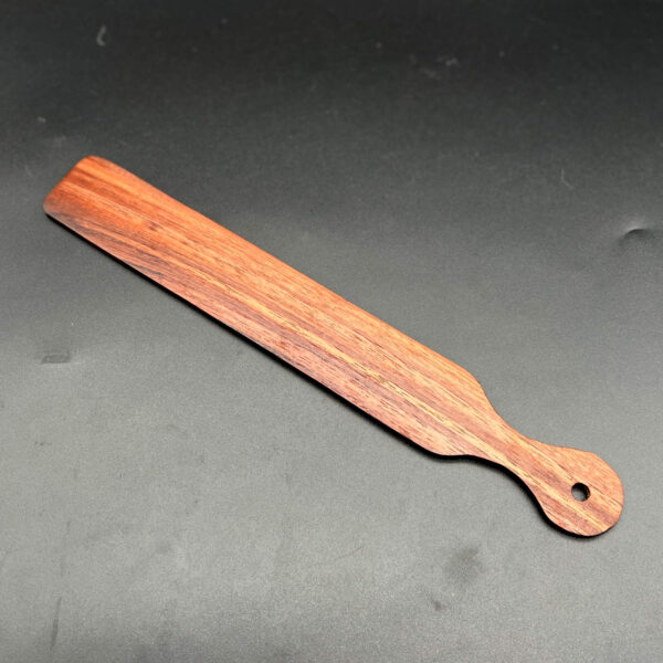Narrow, thin, and long wooden paddle that looks like a ruler or a paint stir stick made in Black Walnut, a deep, dark brown wood