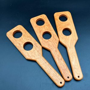 Three Holy Terror paddles made of Cherry. Each paddle has two holes cut through the paddle. 