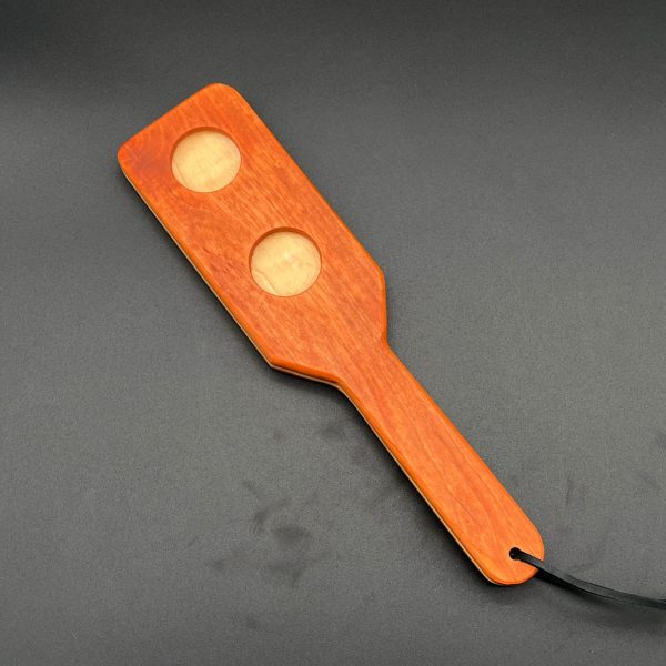 Holy Terror paddle made using three pieces of wood. Cherry wood (red-brown) is on the outside, and Maple (cream-beige) is in the center. Two holes are cut out of one side of the paddle.