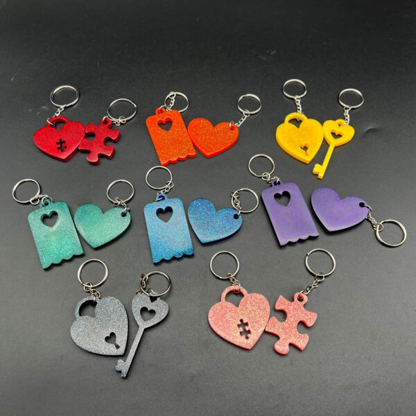Group picture of keychain sets representing all the available colors. Top row, left to right: Red puzzle set, orange heart set, yellow key set; Middle row, left to right: green heart set, blue heart set, purple heart set; Bottom right, left to right: black key set, pink puzzle set