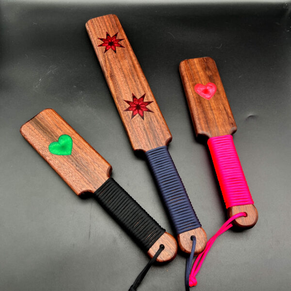 a variety of Resin Inlay paddles in Black Walnut -- from right to left, small with green heart, large with two 8-point stars in red, and small with pink heart