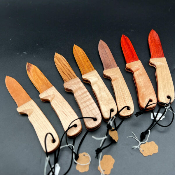 multiple wooden knives, all made with maple handles. The blades, from left to right: cherry, honey locust, zebrawood, black walnut, paduak, and bloodwood