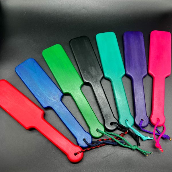 Multiple wooden paddles stained in a variety of colors. From left to right: red, blue, green, black, turquoise, purple, and pink