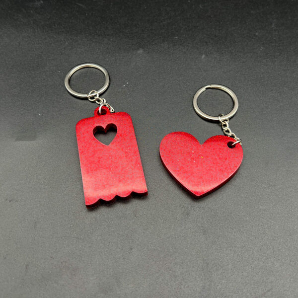 Two keychains made with red resin and glitter. On the left is a rectangular keychain with a scalloped bottom and a heart cut out at the top. On the right is a heart. Both have silver keychain hardware.